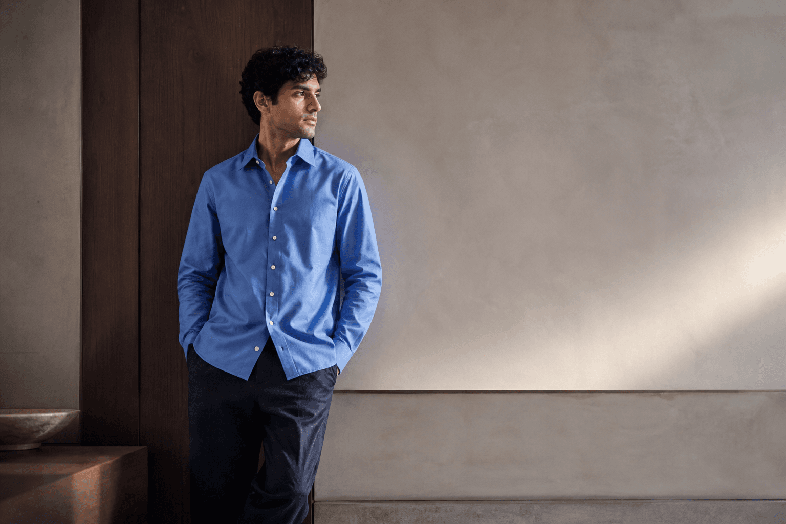 South Asian man in a crisp washed-blue cotton poplin shirt and ink twill trousers